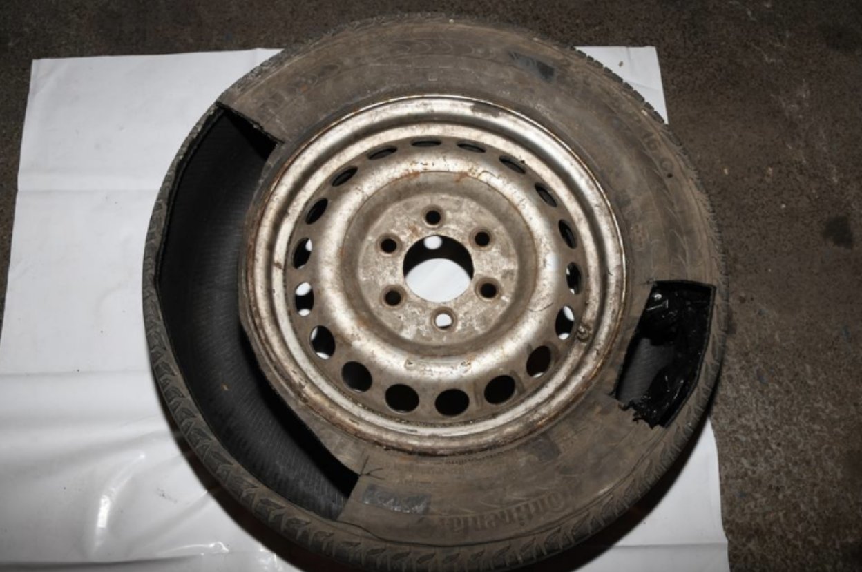 Rusty steel car wheel rim with a severely damaged tire showing a large cut and exposed inner layers.